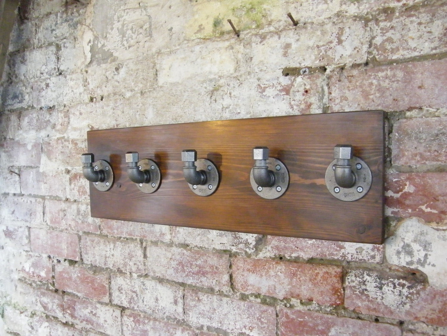 a coat rack using malleable iron pipe fittings, with a walnut style finish backing plate